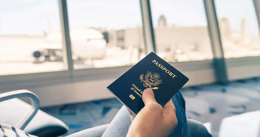 Person holding passport at an international airport departure gate — representing the global freedom that a second passport enables for travel and business